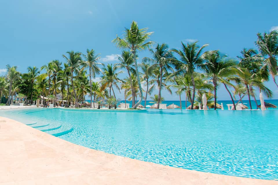 Lagoon-style resort pool with shallow water, palm trees, and tropical beach setting