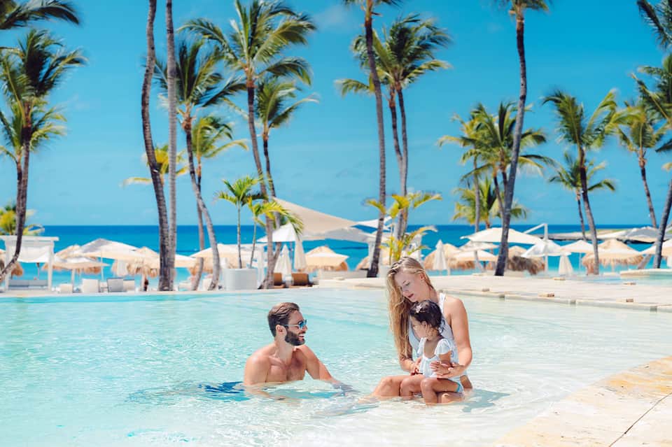 Family enjoying tropical pool with palm trees and beach cabanas in background