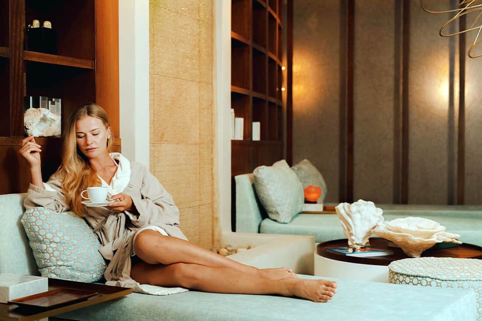 Woman relaxing in luxury spa suite with mint-green furnishings and warm lighting