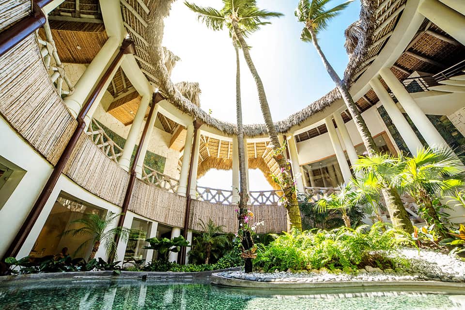 Tropical resort courtyard with circular pool, white buildings, and tall palm trees