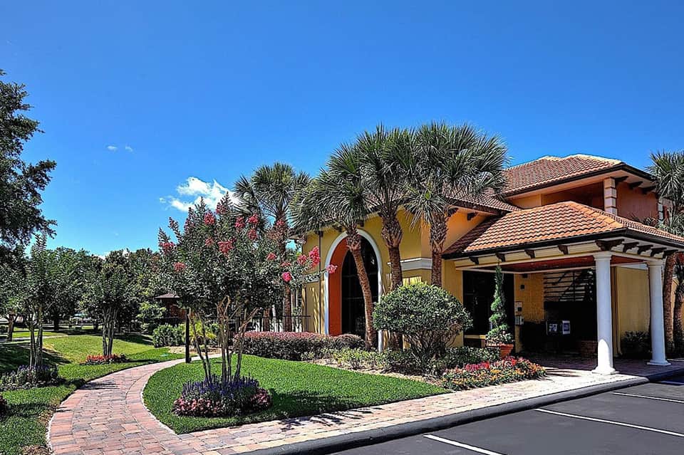 Colorful resort entrance with yellow walls, red accents, palm trees, and manicured grounds