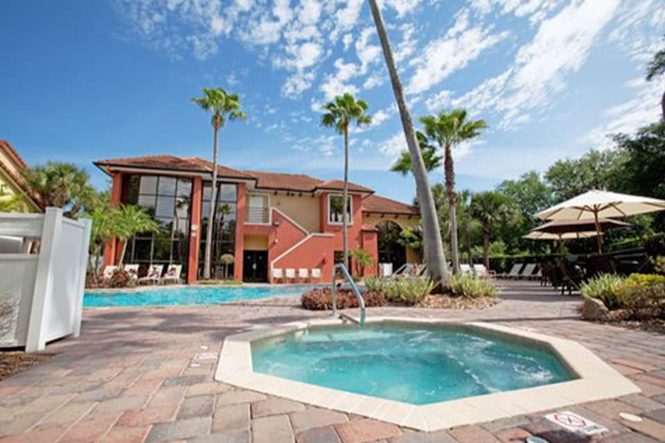 Resort main building with red exterior, pool, spa tub, and palm tree landscaping