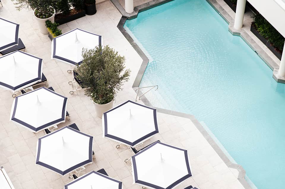 Luxury hotel pool deck with hexagonal white umbrellas and crystal-blue water