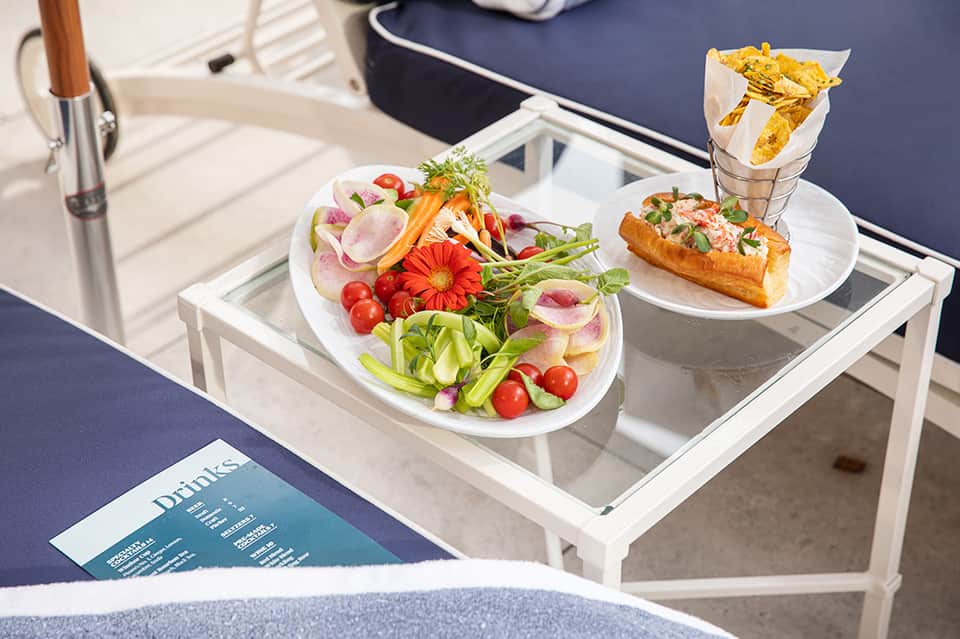 Gourmet salad and sandwich with golden chips on white plates served on pool deck furniture