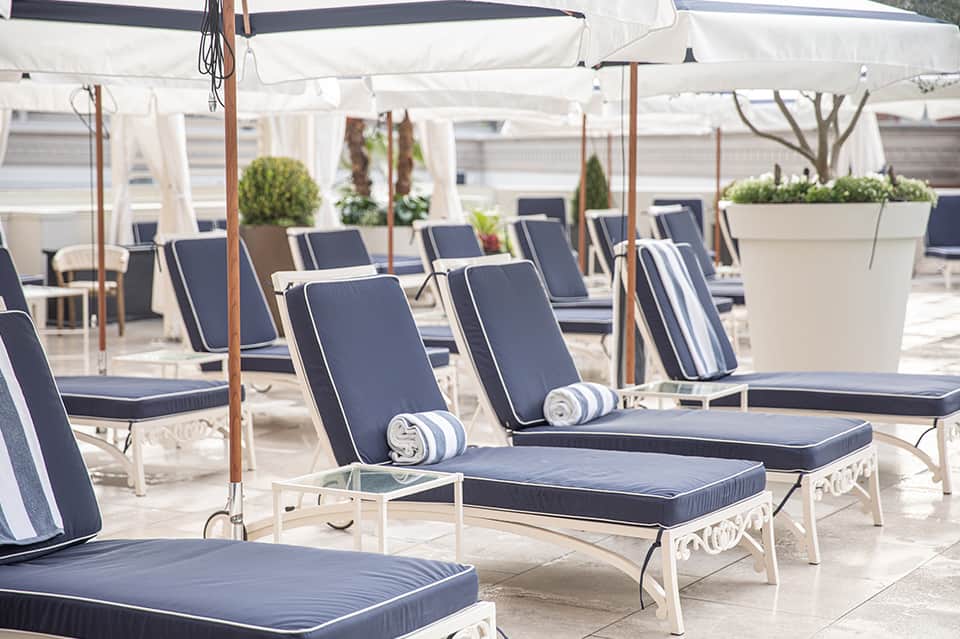 Poolside lounge area with chaise lounges under white umbrellas and striped cushions