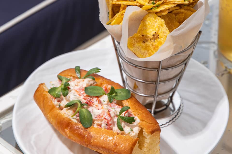 Lobster roll sandwich with fresh herbs and crispy potato chips on white plate