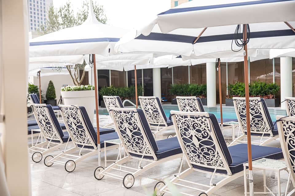 Outdoor pool area with white umbrellas, ornate lounge chairs, and manicured landscaping