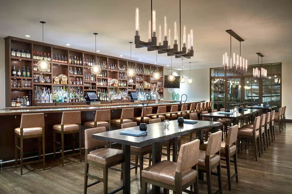 Upscale bar and lounge with dark wood shelving, elegant pendant lighting, and dining tables