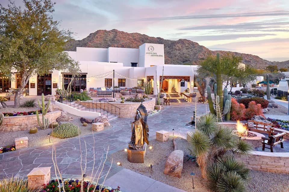 Contemporary white resort building at dusk with desert mountain backdrop and courtyard fire pit