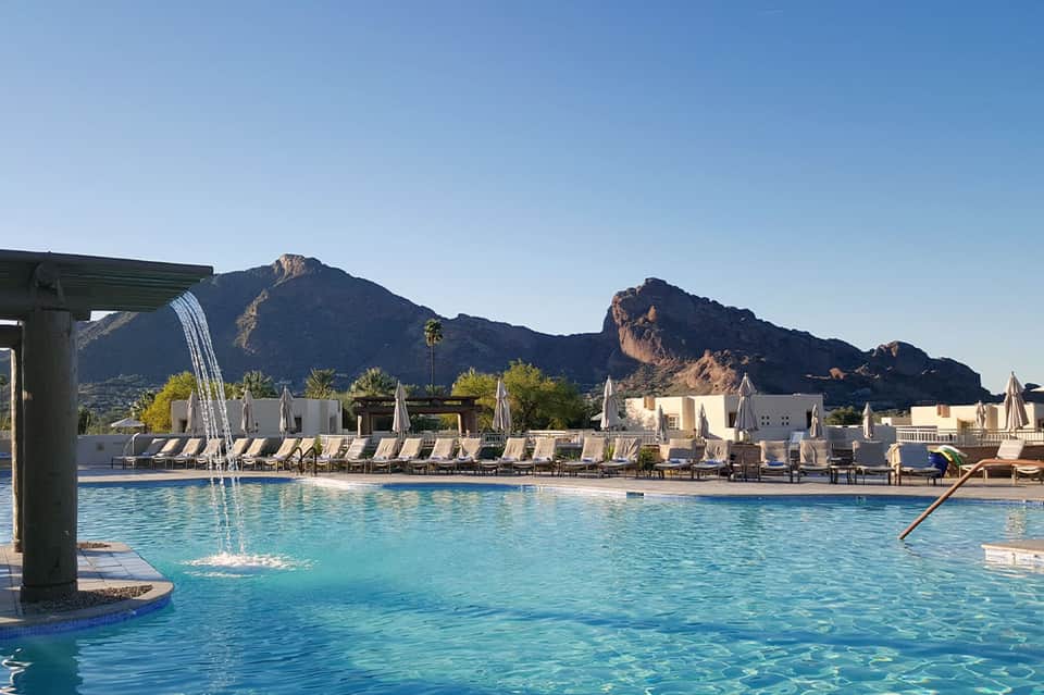 Resort pool with mountain backdrop, white lounge chairs, and cabanas in desert setting