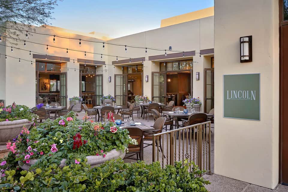Lincoln restaurant courtyard with flowering planters, string lights, and patio dining chairs at dusk