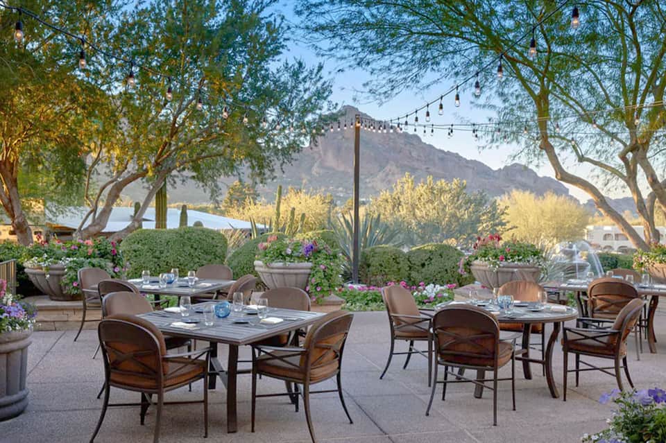 Outdoor patio restaurant with tables under tree canopy and mountain views at dusk