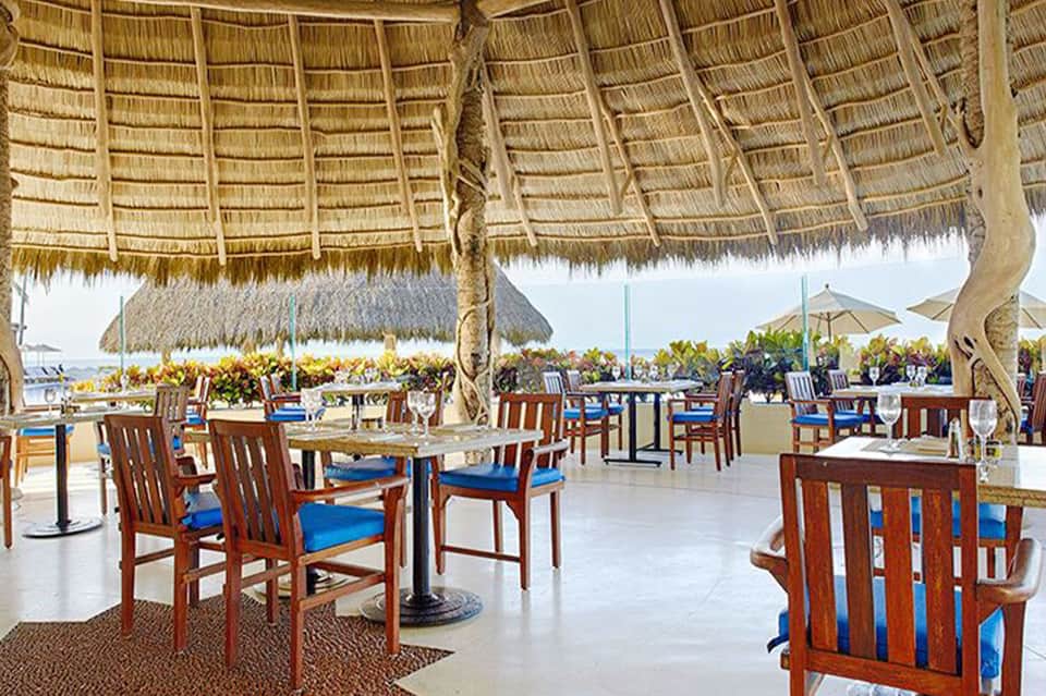 Thatched-roof beachfront restaurant with wooden chairs and ocean view