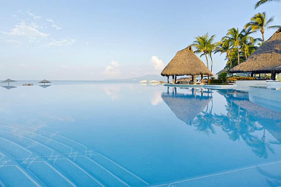 Infinity pool reflecting sky with thatched cabana and calm ocean view