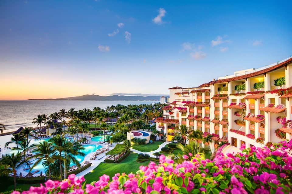 Beachfront resort at sunset with colorful buildings, pools, palm trees, and ocean view