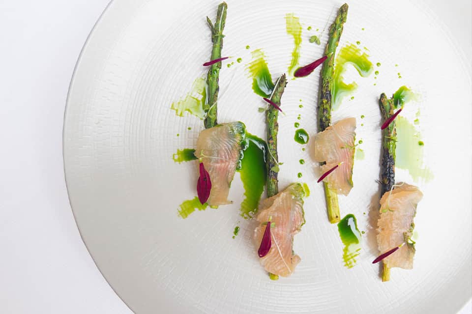 Gourmet plated dish with asparagus, smoked salmon, and green sauce on white plate