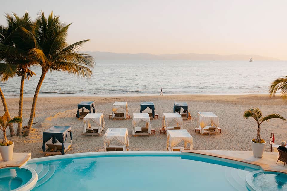 Beach cabanas with white canopies arranged on sand facing ocean at sunset