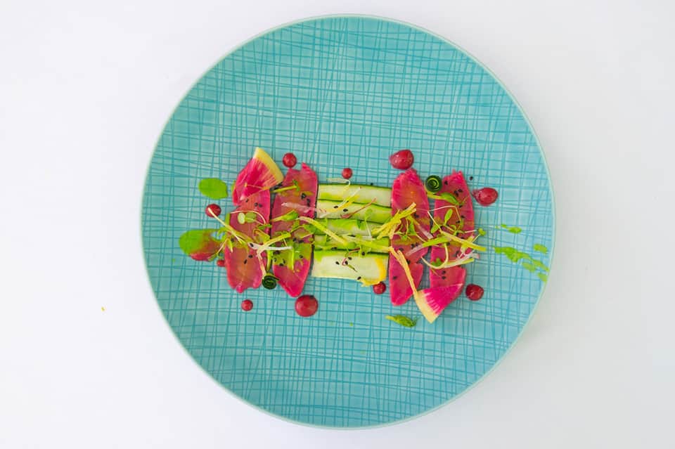 Plated dish with dragon fruit, green vegetable, and red berries on turquoise textured plate