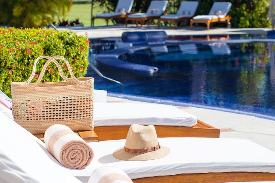 Poolside loungers and beach bag with hat and rolled towel overlooking resort pool and grounds