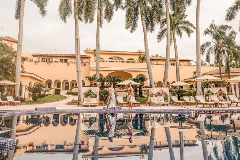 Luxury resort courtyard with tall palm trees, arched architecture, guest lounging by reflecting pool