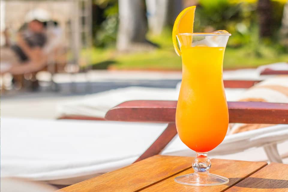 Tropical cocktail with orange juice and lemon slice on poolside table