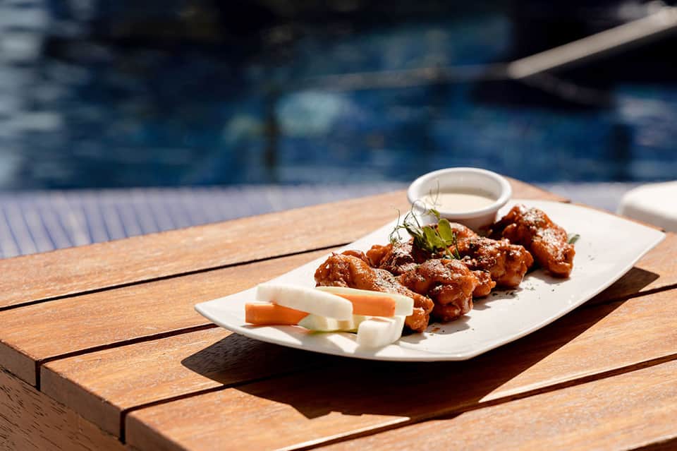 Spicy chicken wings appetizer with ranch dip on wooden poolside table