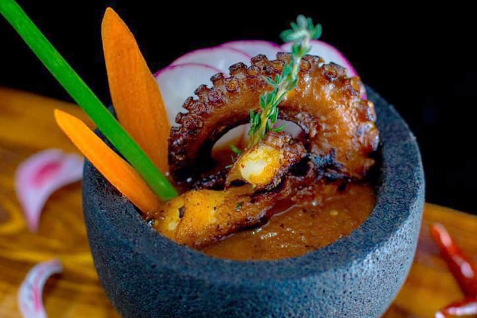 Gourmet octopus dish presented in slate bowl with colorful vegetable garnish