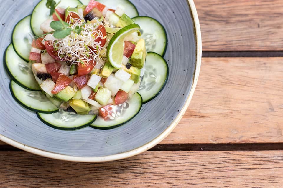 Artfully plated salad with cucumber slices, fresh vegetables, and lime garnish on wood table