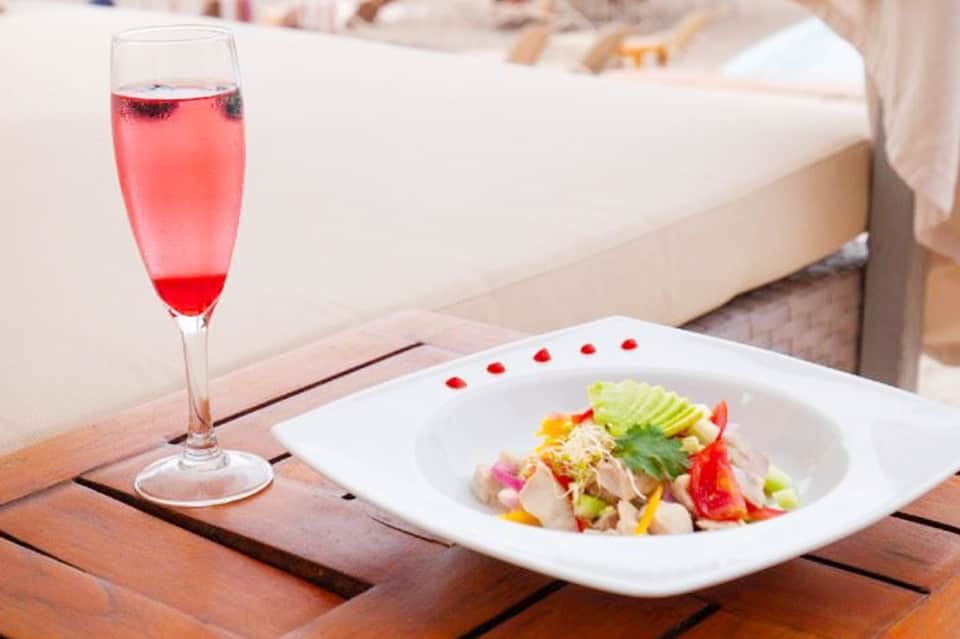 Gourmet plated salad and pink cocktail on wooden table overlooking beach