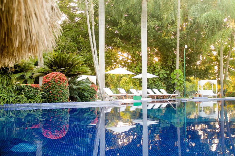 Resort infinity pool overlooking tropical landscape with lounge chairs, umbrellas, and palm trees