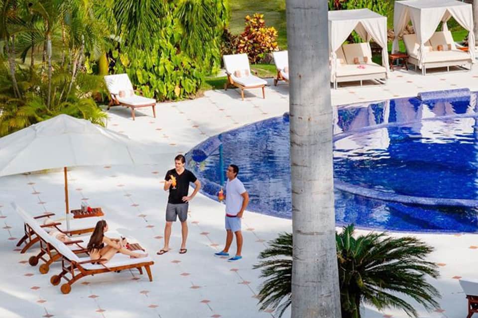 Resort pool area with white cabanas, lounge chairs, and tropical landscaping
