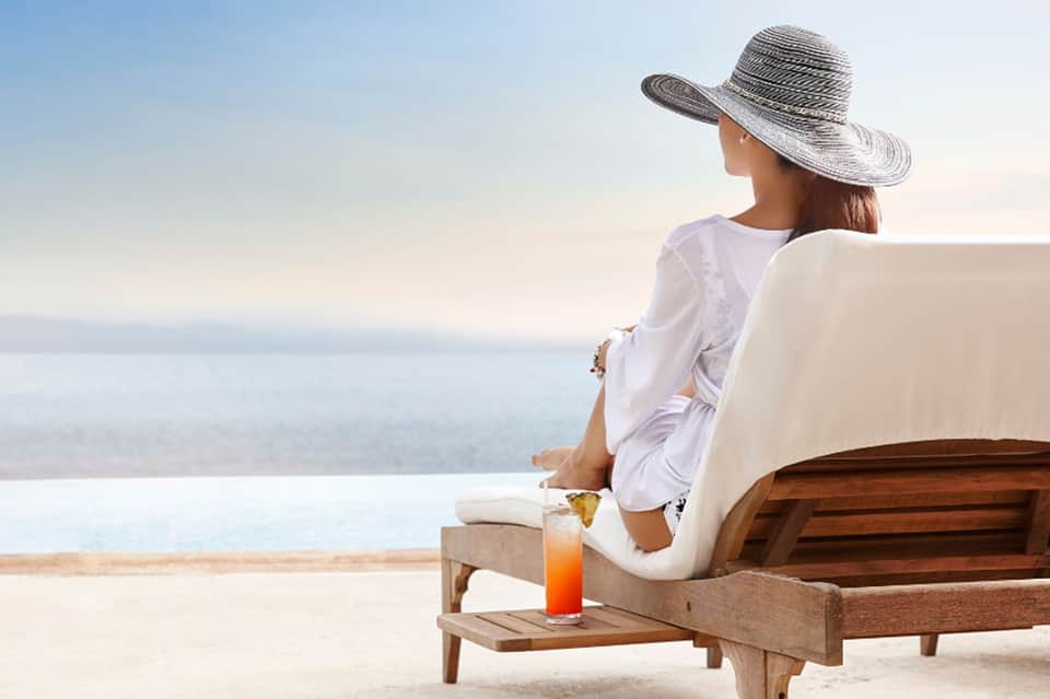 Woman relaxing on beach lounge chair overlooking calm ocean waters at sunset