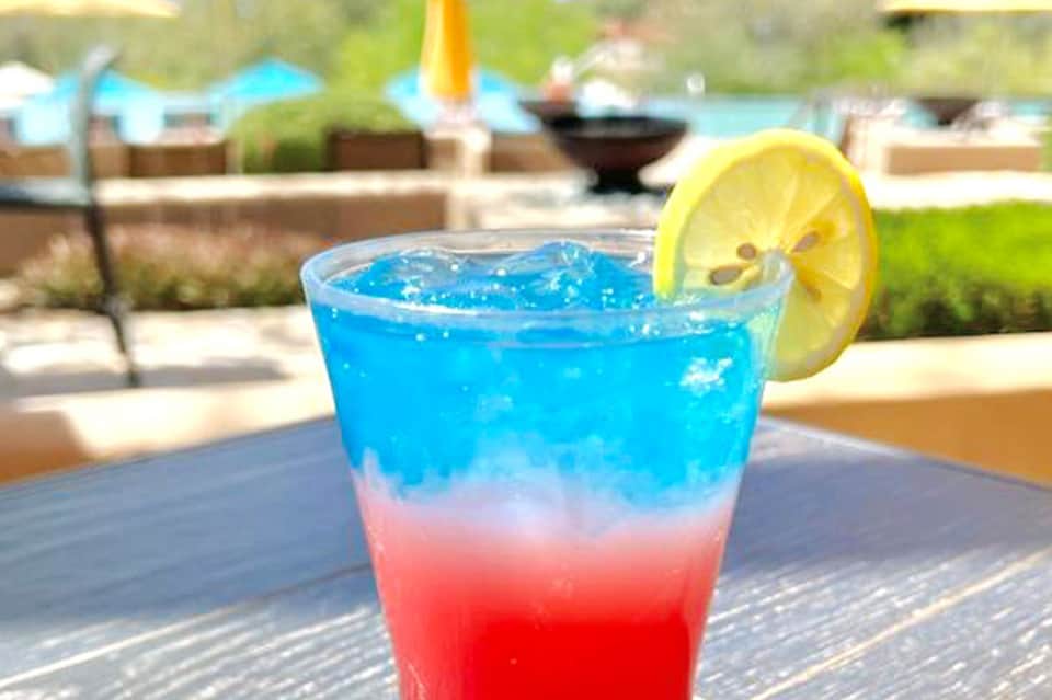 Colorful layered cocktail with lemon slice at poolside resort setting