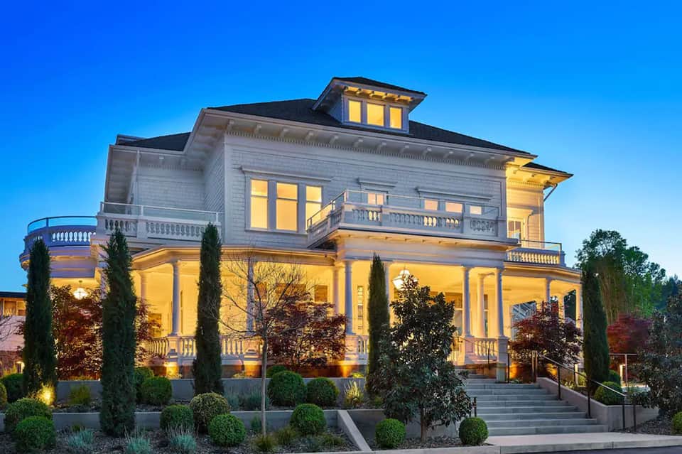 Illuminated white historic mansion at dusk with manicured landscaping and columned portico