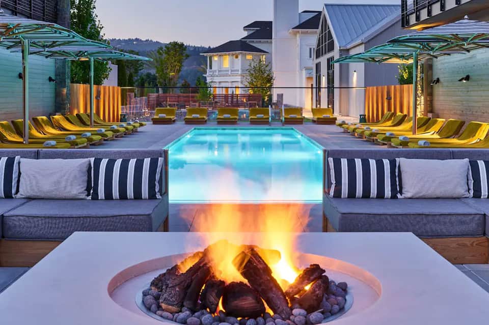 Resort pool at dusk with illuminated water, fire pit, yellow loungers, and modern architecture