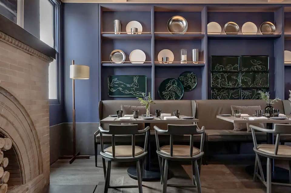 Contemporary restaurant dining area with blue-gray walls, booth seating, and decorative shelving