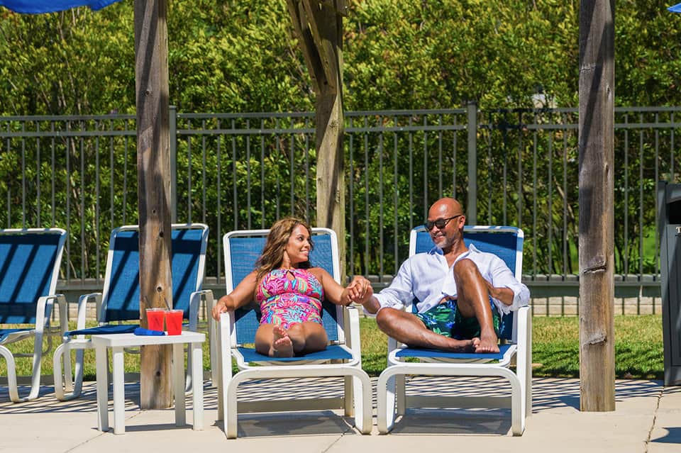 Couple relaxing on lounge chairs under pergola with river and green vegetation in background