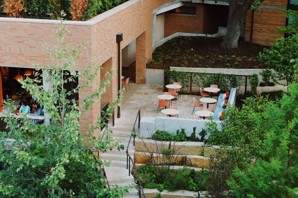 Outdoor courtyard with brick architecture, dining tables, and lush green landscaping