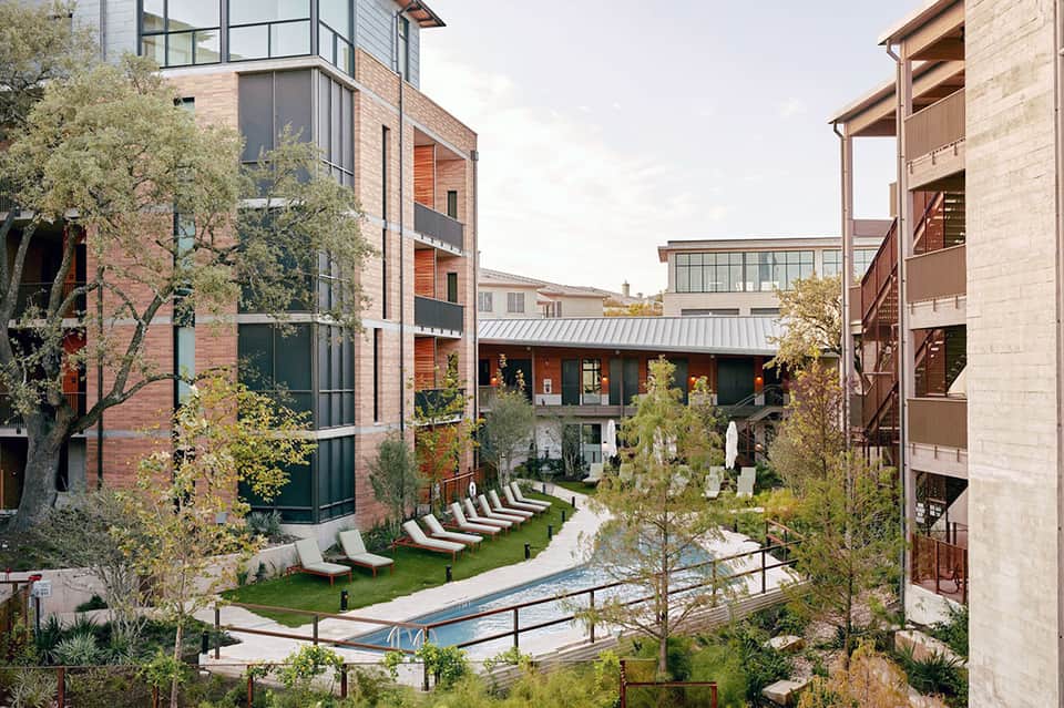 Contemporary resort courtyard with lounge chairs, swimming pool, and multi-story brick buildings
