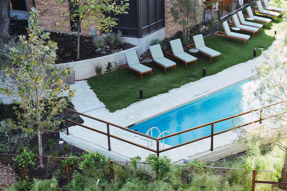 Modern pool area with lounge chairs and grass, backed by contemporary building with black windows