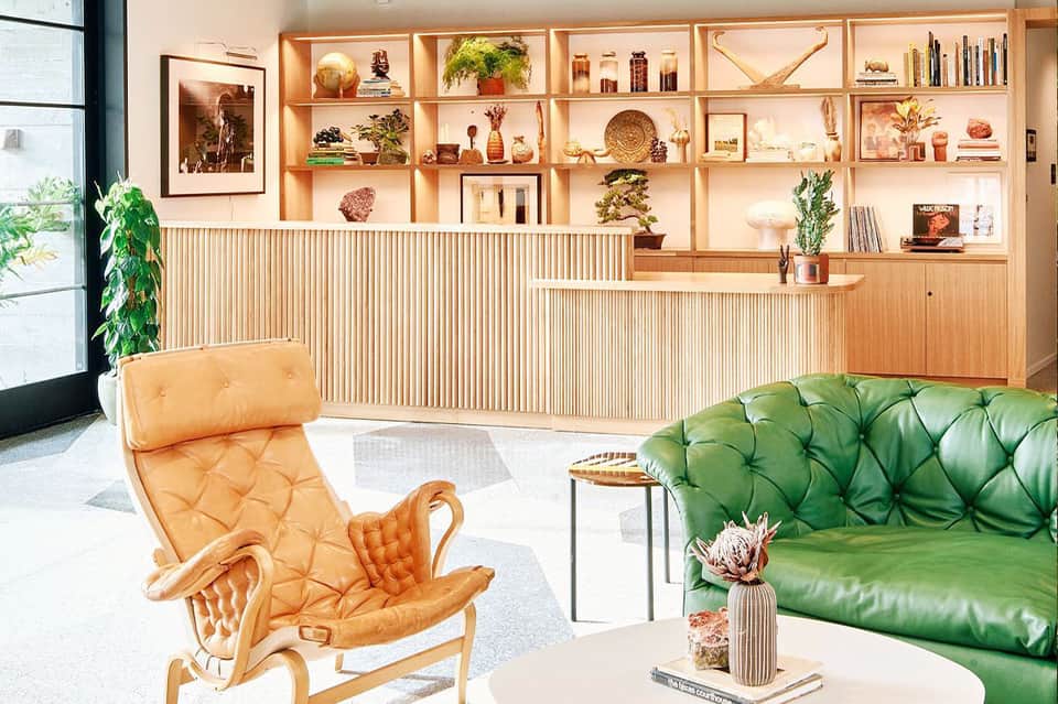 Luxury lounge with green leather sofa, tan leather chair, wooden shelving, and warm ambient lighting