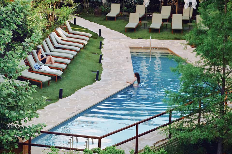 Resort pool surrounded by lounge chairs on green lawn with lush landscaping and stone pathways