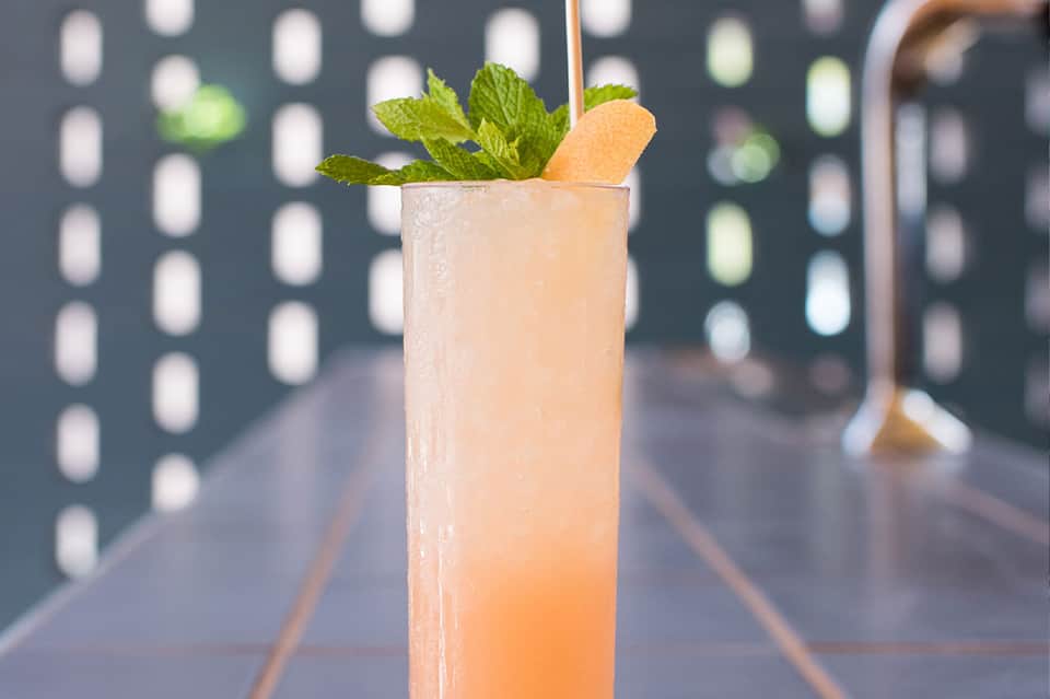 Pale peach cocktail with fresh mint and wafer cookie garnish on a blurred background