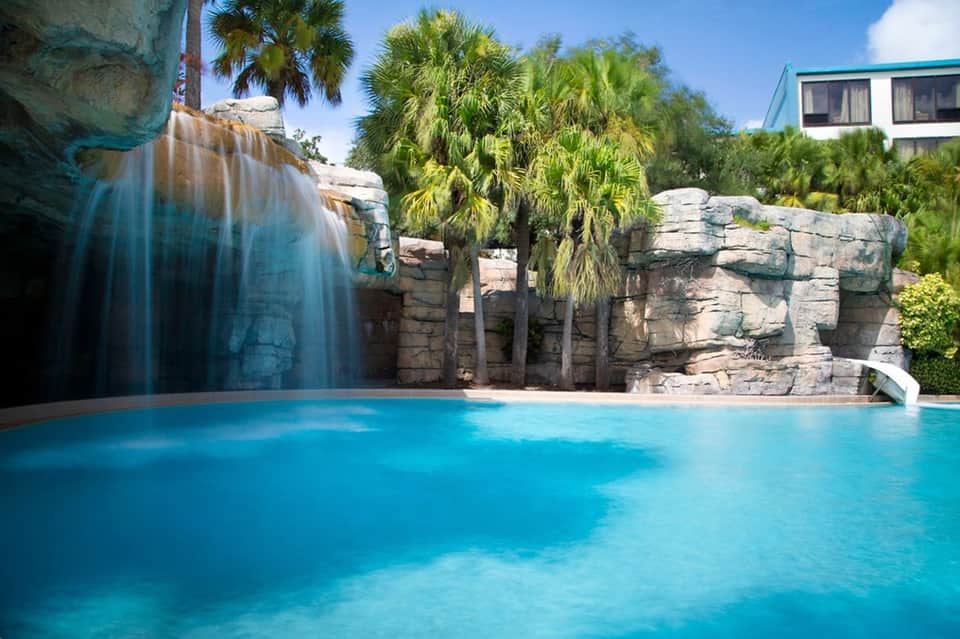 Luxury pool with waterfall feature and palm trees surrounded by rock formations
