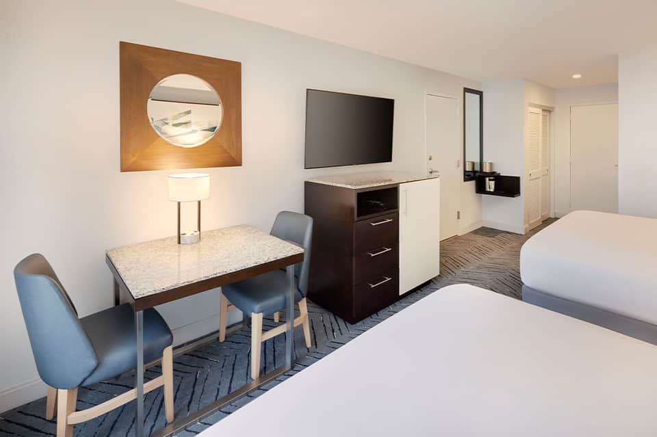 Modern hotel room with two queen beds, work desk, flat-screen TV, and contemporary furnishings