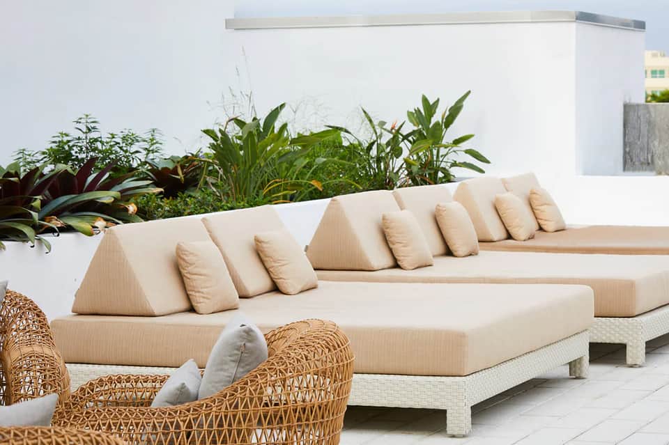 Modern outdoor lounge with cream sectional sofa and tropical plants beside white wall