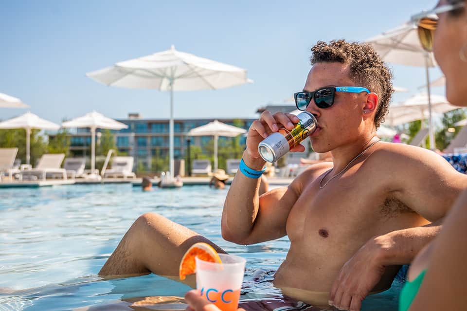 Man in swimming pool enjoying beverage with resort umbrellas and buildings behind