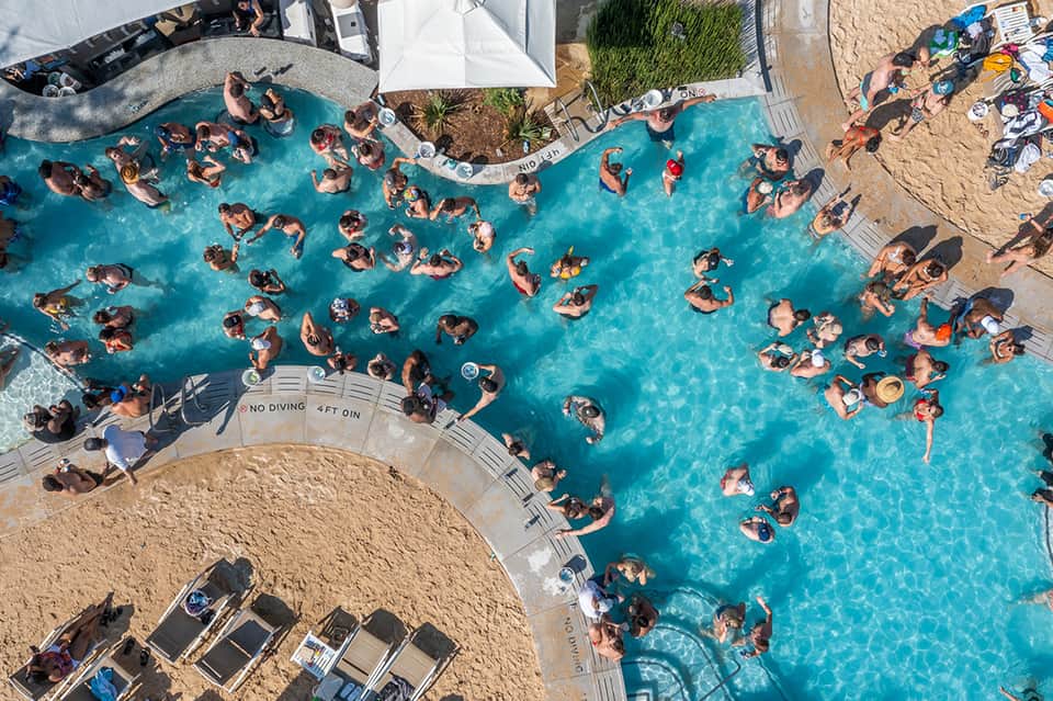 Overhead view of crowded resort pool with dozens of guests swimming and sunbathing