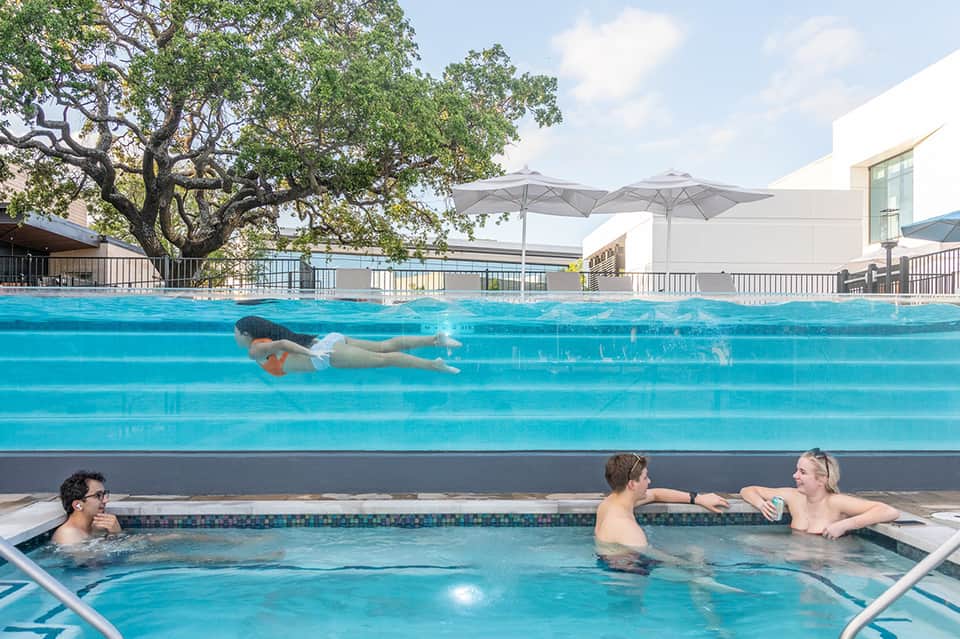 Swimmer doing freestyle strokes in lap pool with hot tub and umbrellas nearby