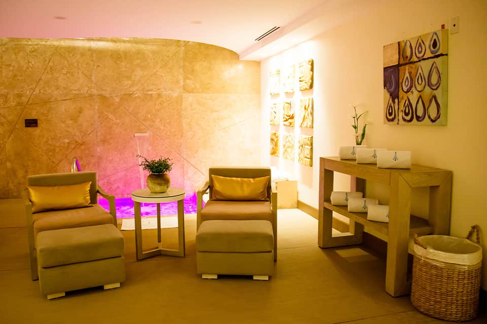 Spa relaxation room with warm golden lighting, cream chairs, wood furnishings, and decorative wall art